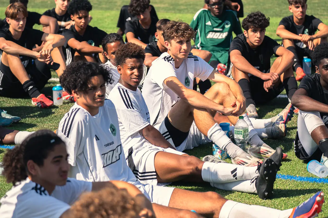 Young players sitting on the pitch, listening during a session.
