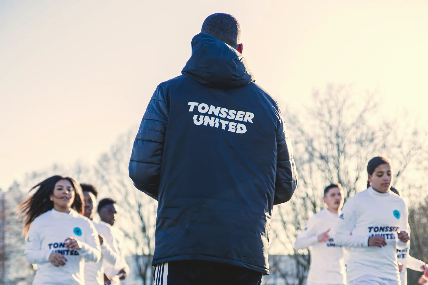 A Tonsser United coach, seen from behind, watching his players warm up.